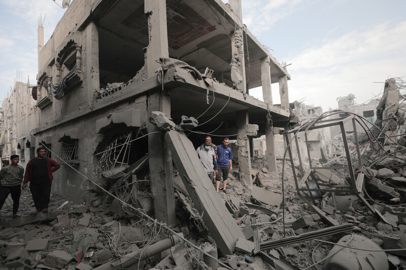 Five men and boys stand next to a totally bombed-out two-story home surrounded by debris and other destroyed buildings
