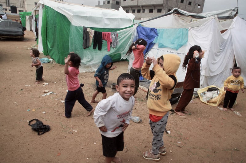 Children smiling as they play in front of tents 