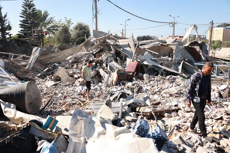 Two men walk amid rubble and remnants of personal belongings