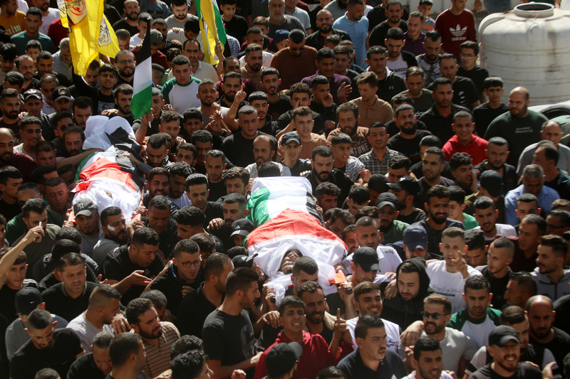 A massive crowd of people carries two bodies wrapped in flags 