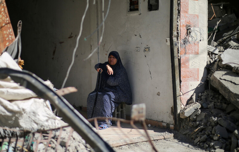 A woman sits by a wall surrounded by rubble