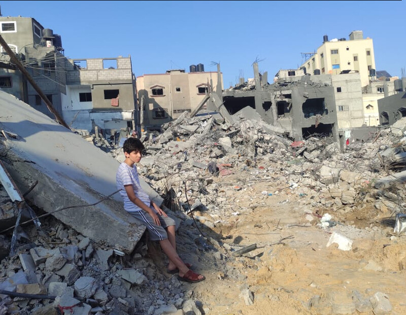 A boy sits looking at rubble