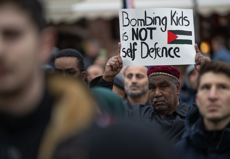 A man holds a sign reading bombing kids is not self defence