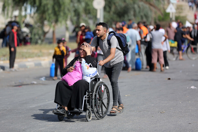 A man pushes a woman in a wheelchair with a group of people on foot behind them