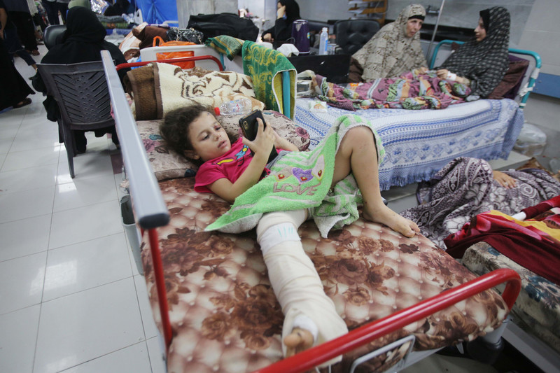 A girls plays on a phone in hospital bed, her leg in plaster