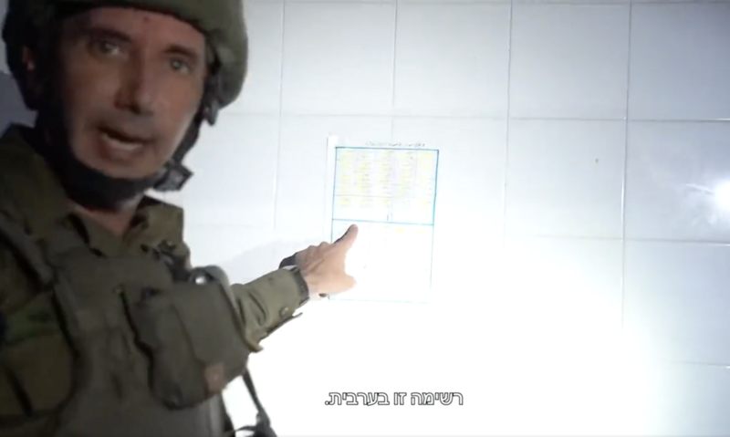Man in military uniform points at sheet of paper taped to tiled wall