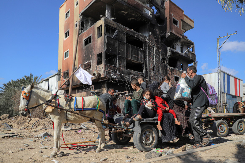 a donkey with a cart crowded with people passing bombed out buildings