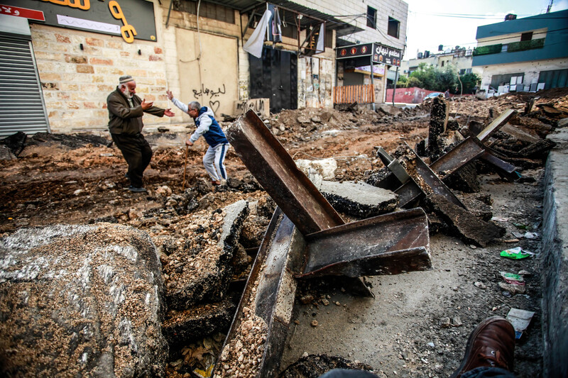 Two men greet on a torn-up road with anti-tank obstacles pushed to the edge of the road