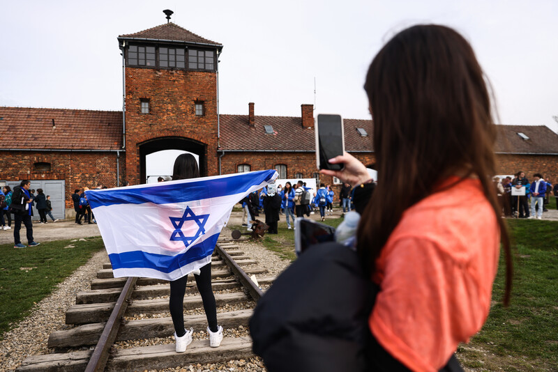 A person carries an Israeli flag in front of a brick building that is part of the former Auschwitz death camp