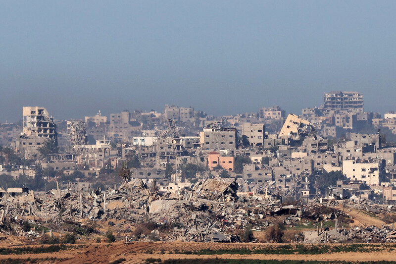 Destroyed buildings in the foreground of densely packed grey cinder-block buildings