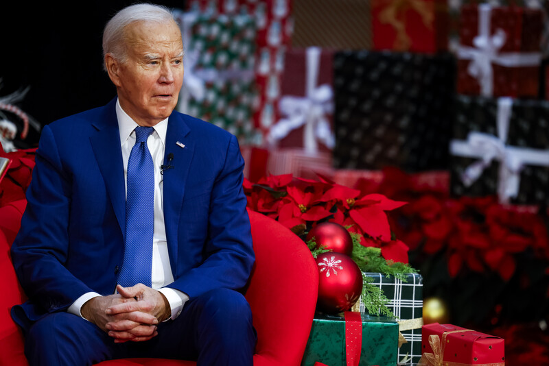 President Joe Biden sits in a red chair with wrapped boxes nearby