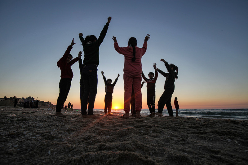 Children jumping together with their arms in the air at sunset on a beach