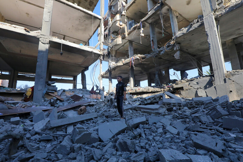 A child standing in rubble between two tall buildings charred and with walls blown out