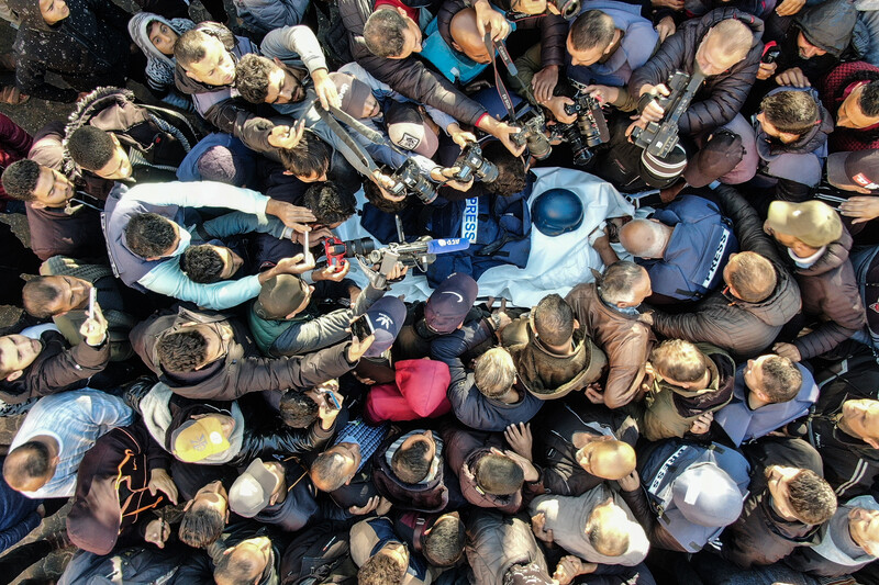 A crowd seen from above surrounds a stretcher with a press helmet