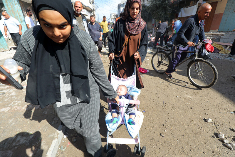 Two women push a stroller through crowded streets.