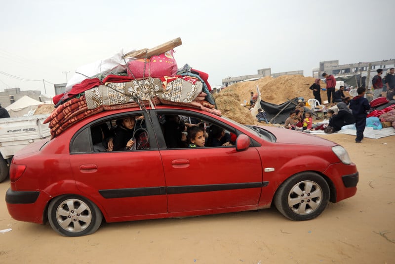 Palestinians in a red car loaded on top with mattresses and other supplies