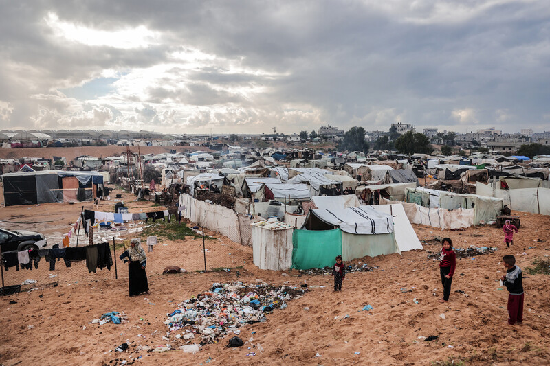A mother and her children stand talking with rows of tents into the horizon