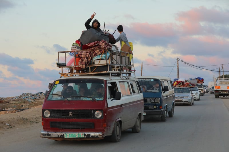 A car loaded with belongings with children on the roof giving a victory sign