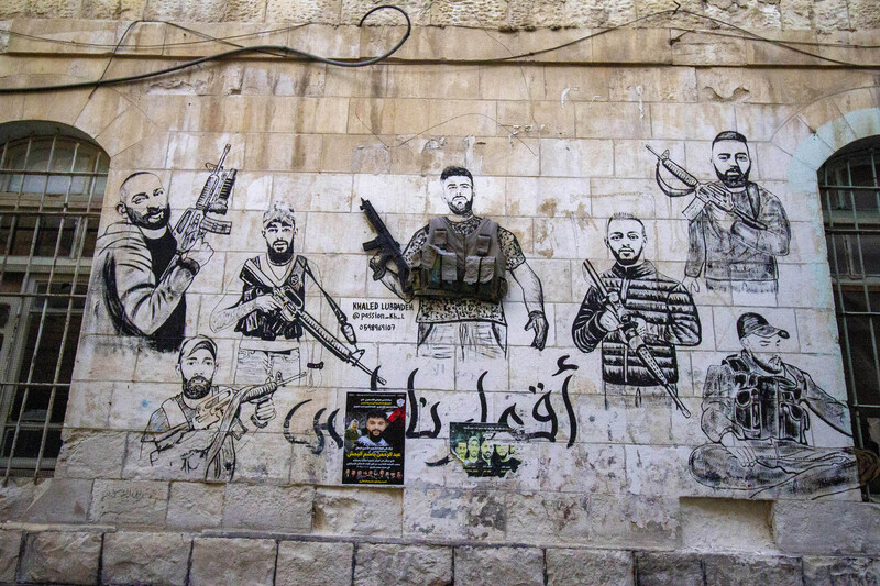 A mural depicting seven armed men is on the stone wall of a building 