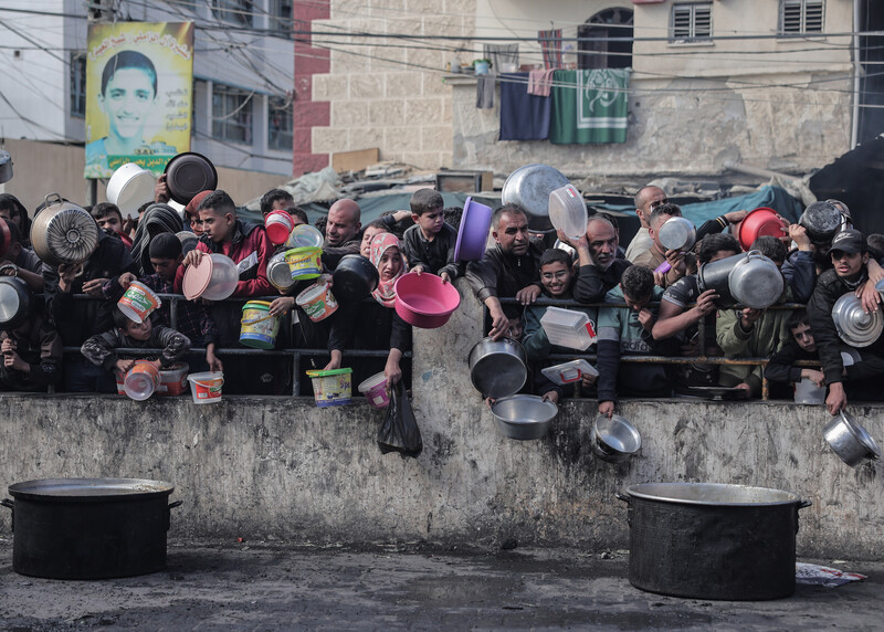 People stand behind a short wall, holding containers to collect food 