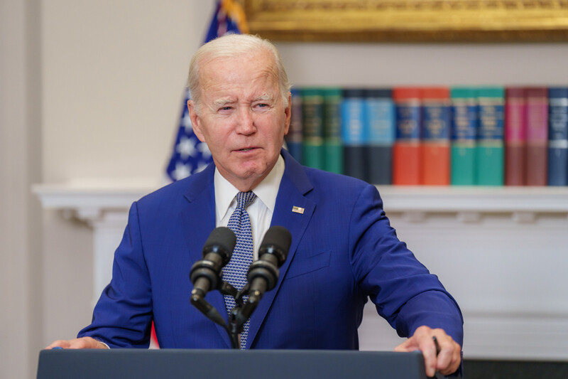 A man in a blue suit stands behind a podium with two microphones