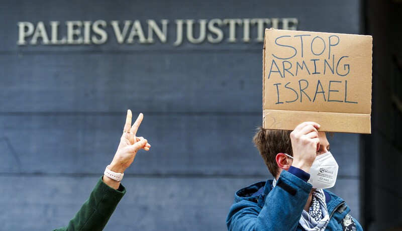 Man holds sign saying stop arming Israel outside court building while another person makes victory sign