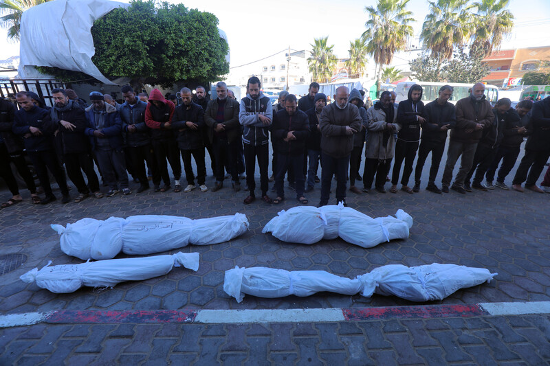 A group of mourners pray over four bodies wrapped in white body bags