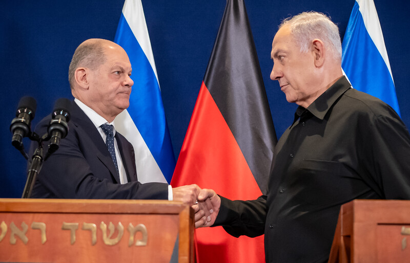 Scholz and Netanyahu shake hands by podiums with Israeli and German flags behind