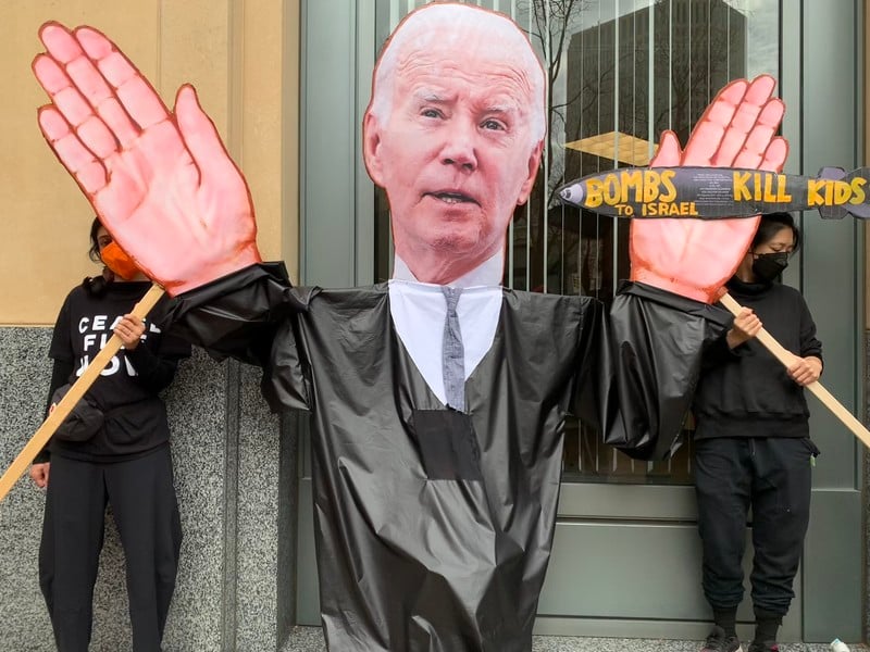 Protesters hold up a giant puppet of Joe Biden with the words "bombs to Israel kill kids" painted on a missile in the puppet's hand