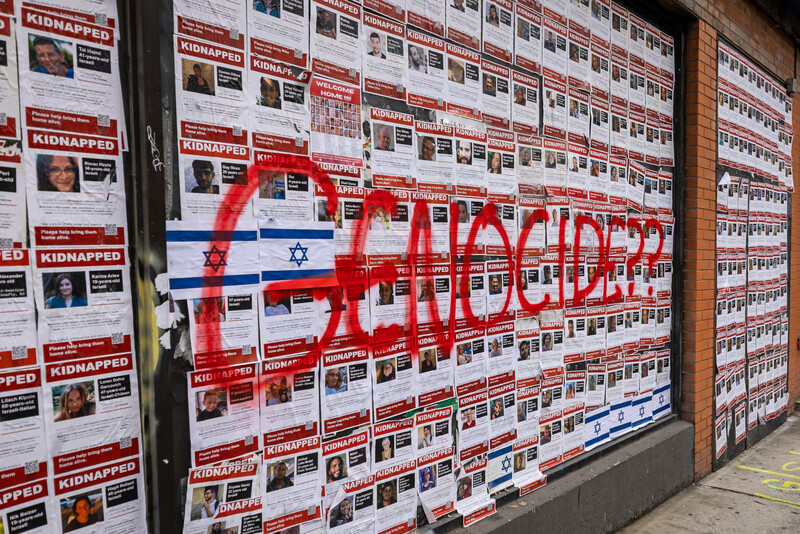 Posters bearing images of Israeli captives in Gaza with the word 'genocide' scribbled across