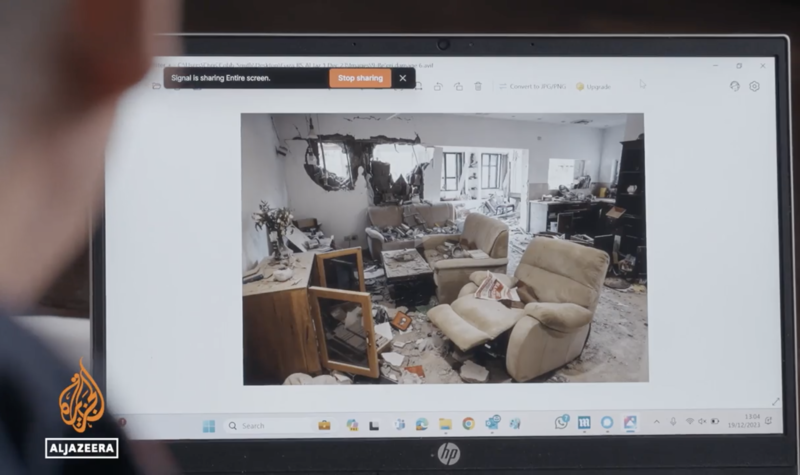 A man with a laptop views an image of a war-ravaged home