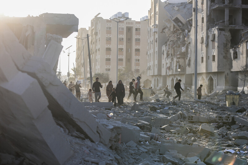 People walk in front of the husks of destroyed buildings