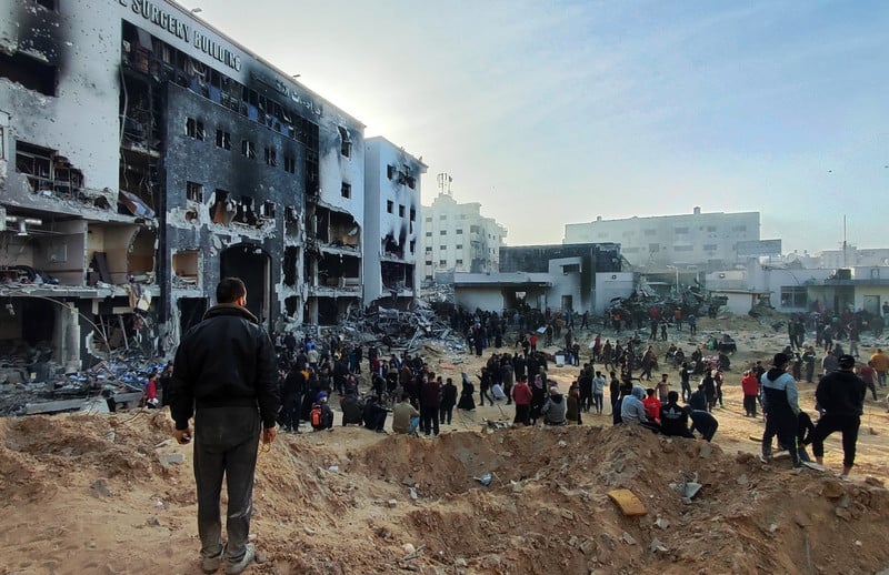 People stand in front of a burned-out hospital building