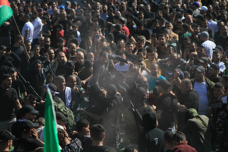 Man is carried on the shoulders of men in a big crowd of people carrying flags and weapons