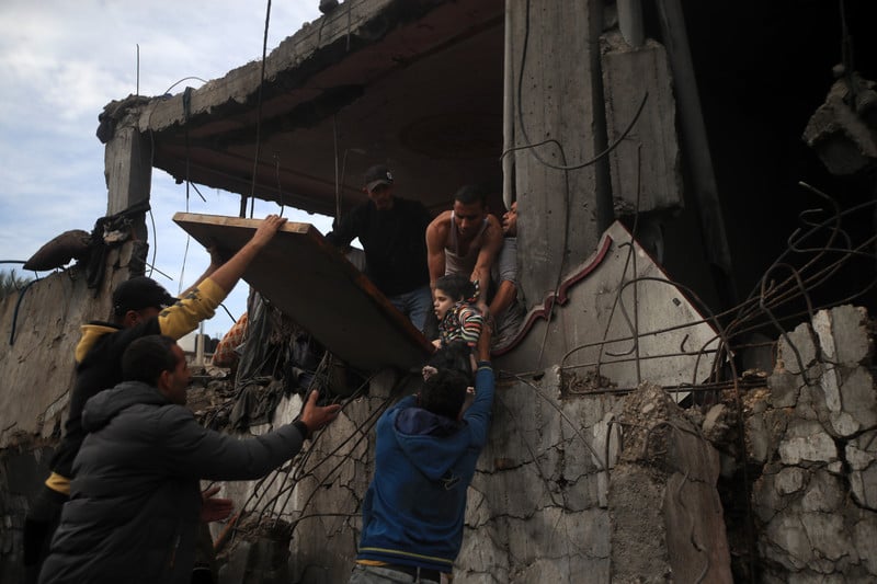 A man standing in a bombed-out building lowers a child to the arms of people standing below
