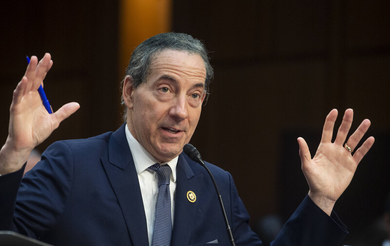 Congressman Jamie Raskin, holding a pen, raises his hands