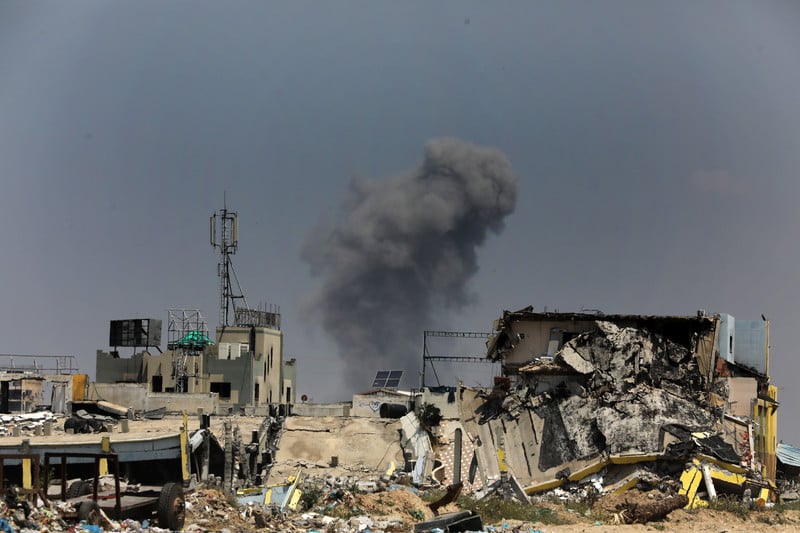 A plume of smoke from an Israeli airstrike rises from a horizon of destroyed buildings