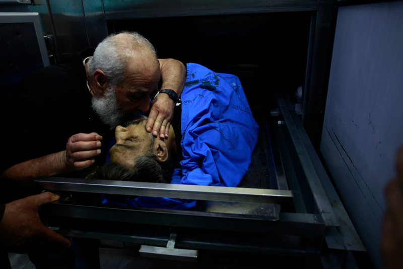 A man leans over to kiss the face of a deceased male inside a hospital morgue refrigerator.