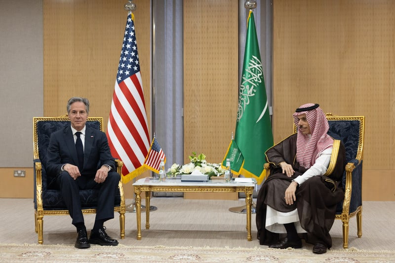Two men sit flanked by the American and Saudi Arabian flags