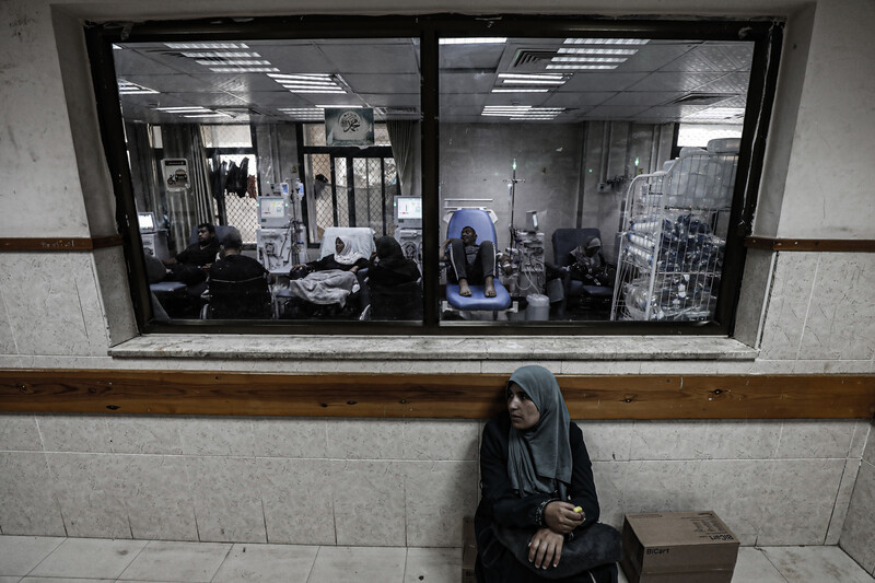 A woman sits below a window to a treatment room