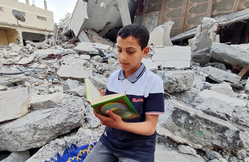 A boy reads a book amid the rubble of a house