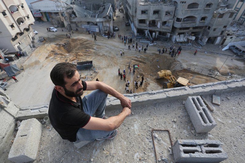 A man sits on a roof inspecting damage after airstrikes