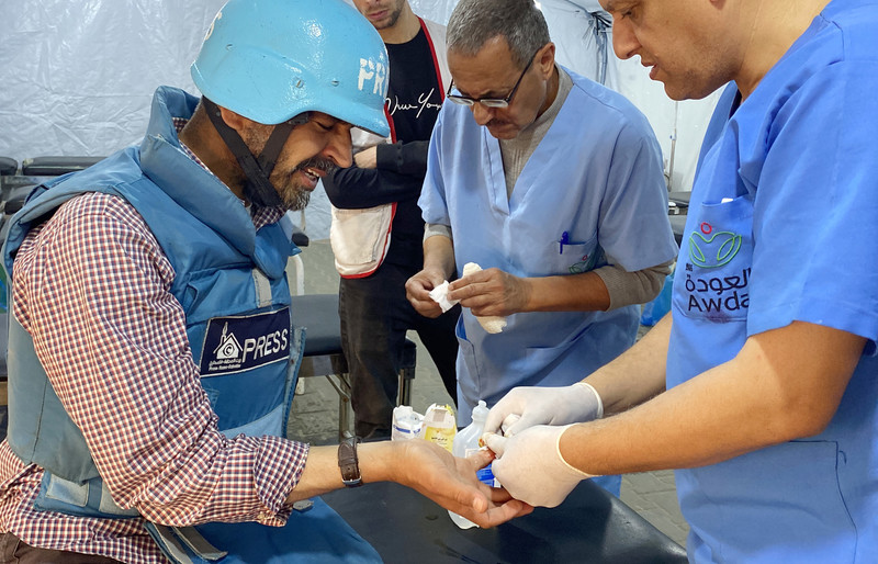 A man in press garb receives treatment from a doctor