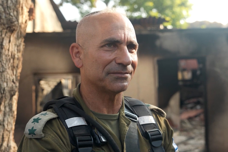 Portrait of smirking man in military uniform in front of burned out house