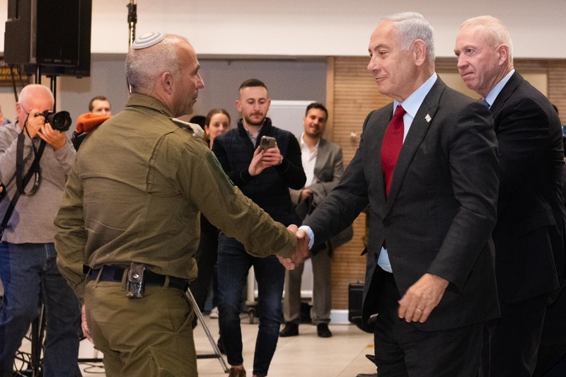 Vach in uniform shakes hands with Netanyahu who is standing in front of Gallant as people look on