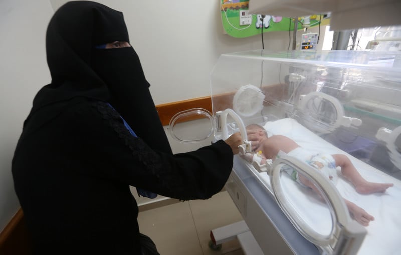 A woman reaches for a baby in a NICU