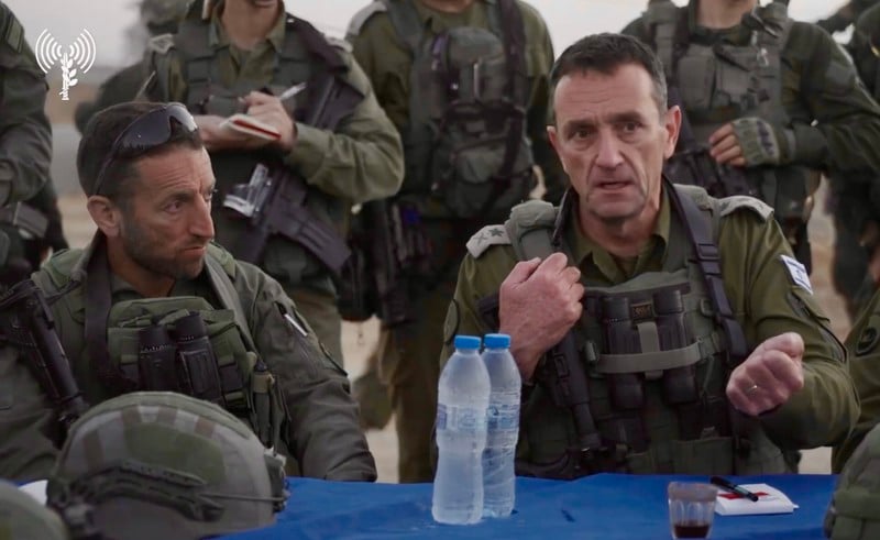 Hiram and Halevi in fatigues seated at table surrounded by armed soldiers