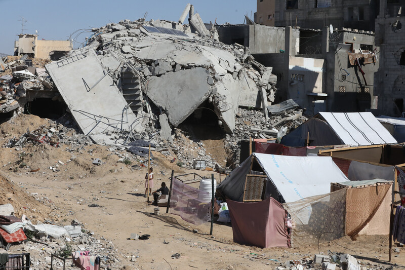 A homemade tent stands next to a destroyed building