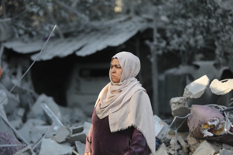 A woman stands in front of the rubble of a house