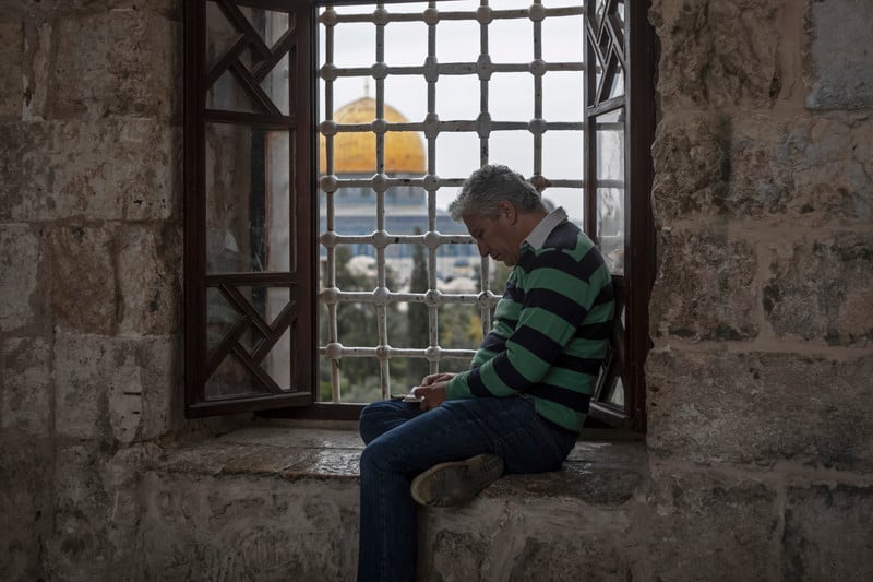 A man sits by a window overlooking the Haram al Sharif